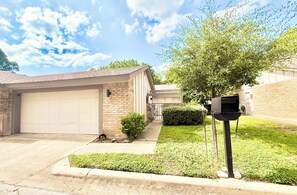 A residential garage with a brick facade, a small front yard with a hedge, and a mailbox. - South Austin Sanctuary Location! Greenbelt, trifold, vaulted, pool, garage, pets (Austin)