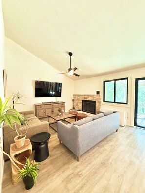 A modern living room with a flat-screen TV, a fireplace, a ceiling fan, and large windows. - South Austin Sanctuary Location! Greenbelt, trifold, vaulted, pool, garage, pets (Austin)