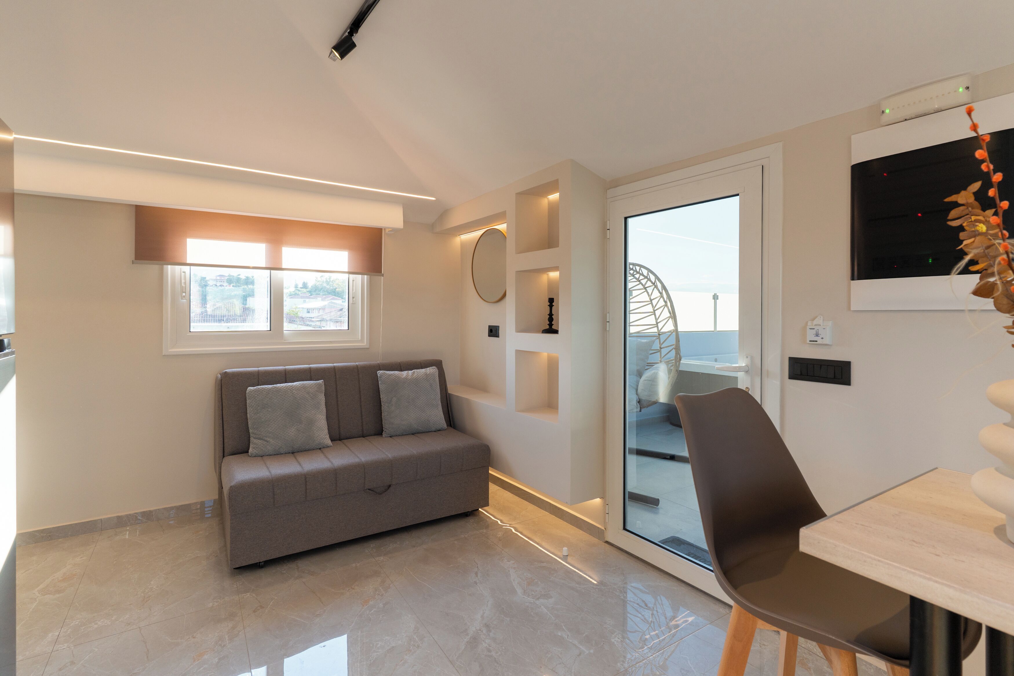 A modern living room with a sofa, a dining table, and a glass door leading to a balcony.