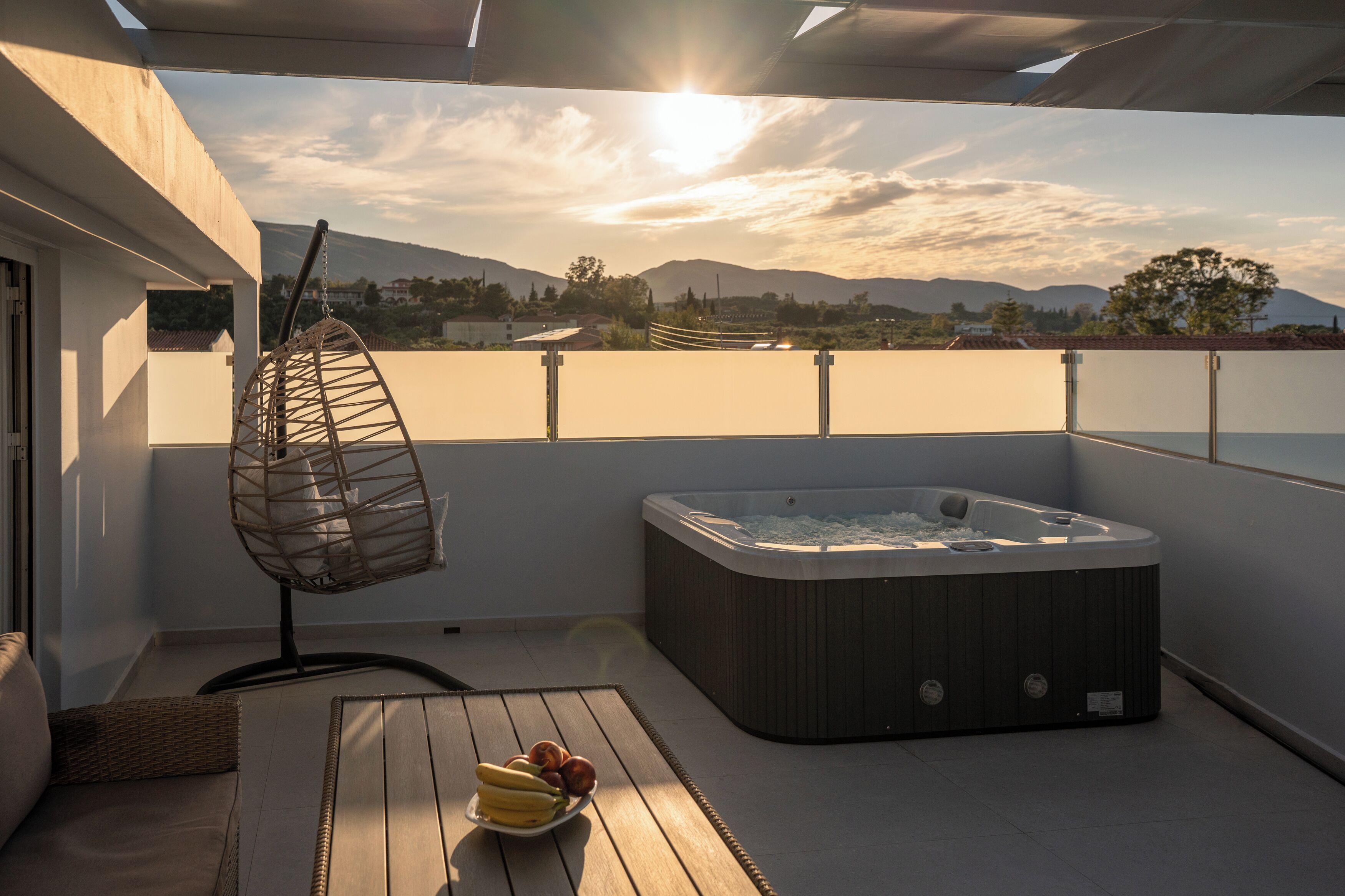 A balcony with a hot tub, a hanging chair, and a table with fruit.