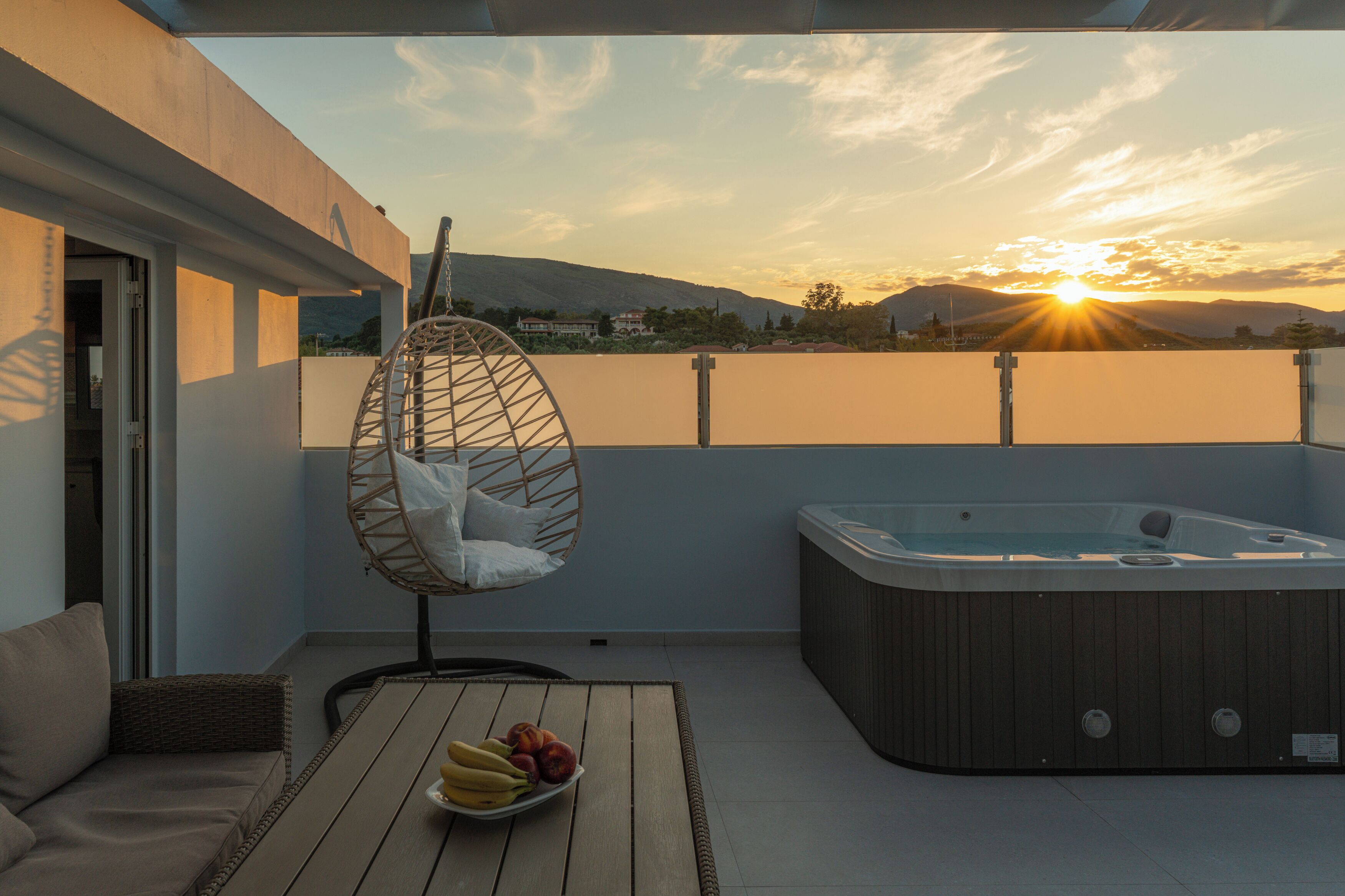 A balcony with a hot tub, a wicker chair, and a table with fruit.