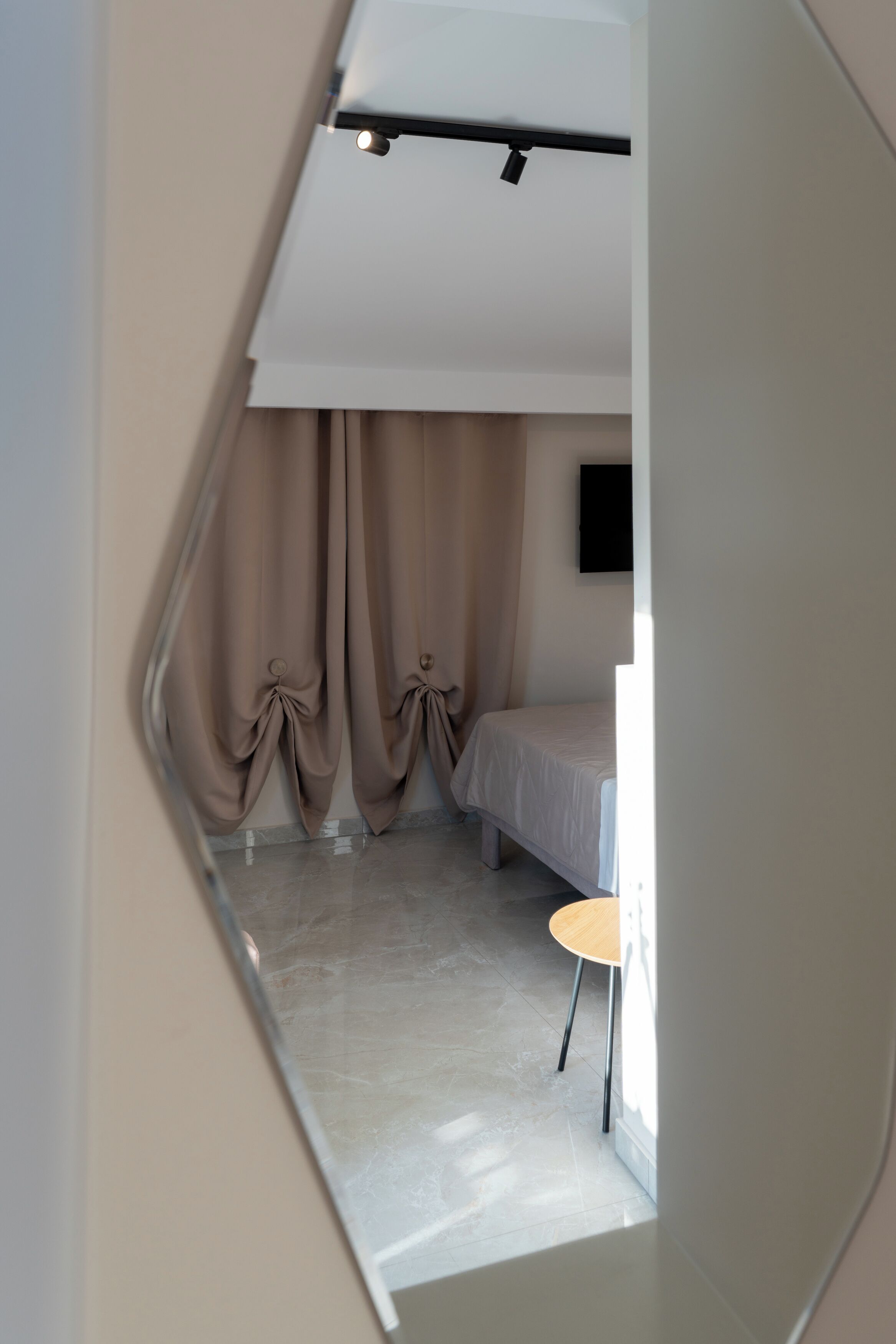 Quarto com uma cama, uma mesinha e cortinas.