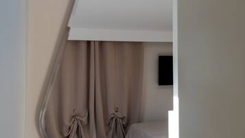Quarto com uma cama, uma mesinha e cortinas.