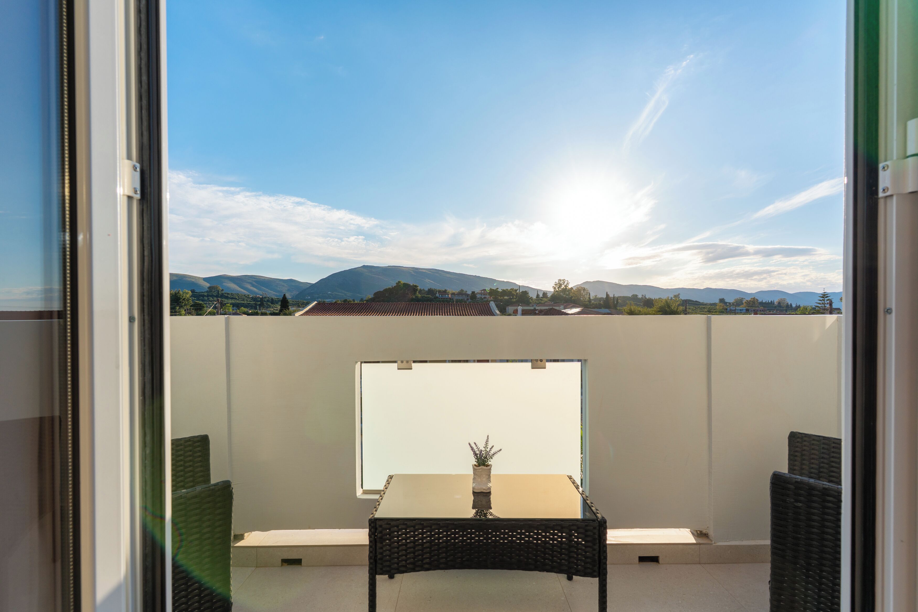 A balcony with a table and chairs, a potted plant, and a view of mountains.