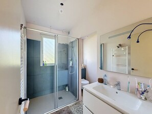 Un baño moderno con mampara de vidrio, lavamanos blanco y espejo con barra para toallas.