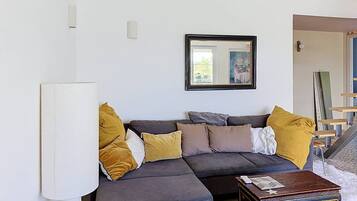 Een woonkamer met een hoekbank, een klein bijzettafeltje en een lijst met een afbeelding.