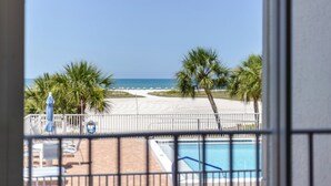 Blick auf einen Strand mit Palmen, einem Pool und Liegestühlen.