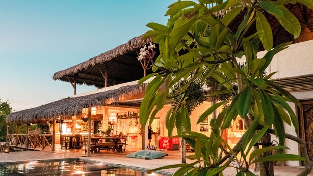 A resort with a pool, outdoor dining area, and a thatched-roof structure.