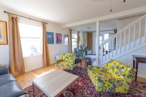Un salon comprenant un canapé, deux fauteuils à motifs, une table basse et un escalier menant à une autre pièce.