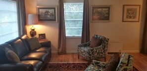 A living room with a leather sofa, a patterned armchair, and a small table with a lamp.