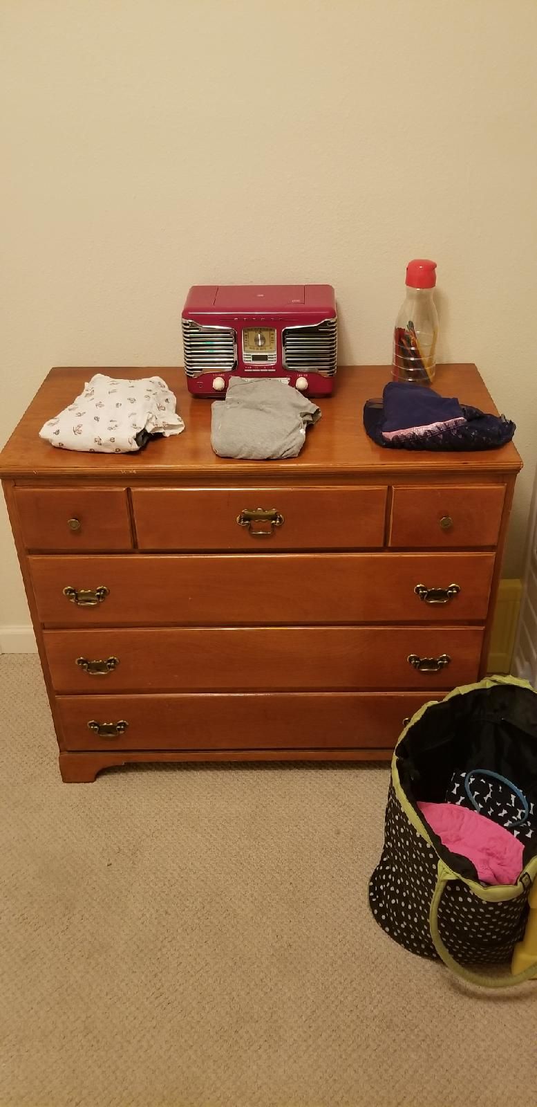 A wooden dresser with drawers, a vintage radio, and a bag with a polka dot pattern.