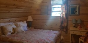 A wooden cabin bedroom with a bed, a nightstand, a lamp, and a dresser. - Vintage 1960s Vibe with Modern Amenities (Prineville)