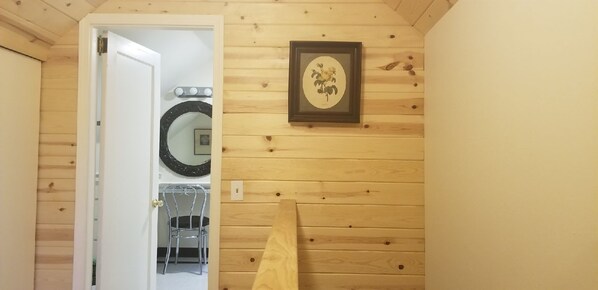 A wooden interior with a door leading to another room, a framed picture on the wall, and a mirror above a chair.