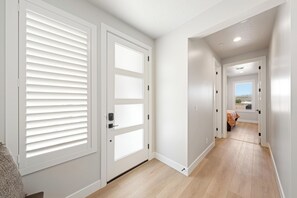 Un pasillo con puertas blancas, una cama a lo lejos y vista al exterior.