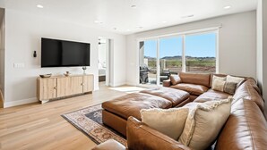 A spacious living room with a large leather sectional sofa, a flat-screen TV mounted on the wall, and a large sliding glass door leading to an outdoor patio. - Isle B there 4U- Private Hot Tub|ResortPool|GolfCourse|Sleeps20 Mins to Canyon (Washington)