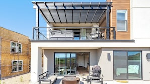 A modern two-story house with a balcony, a patio with outdoor furniture, and a sliding glass door leading to an interior space. - Isle B there 4U- Private Hot Tub|ResortPool|GolfCourse|Sleeps20 Mins to Canyon (Washington)