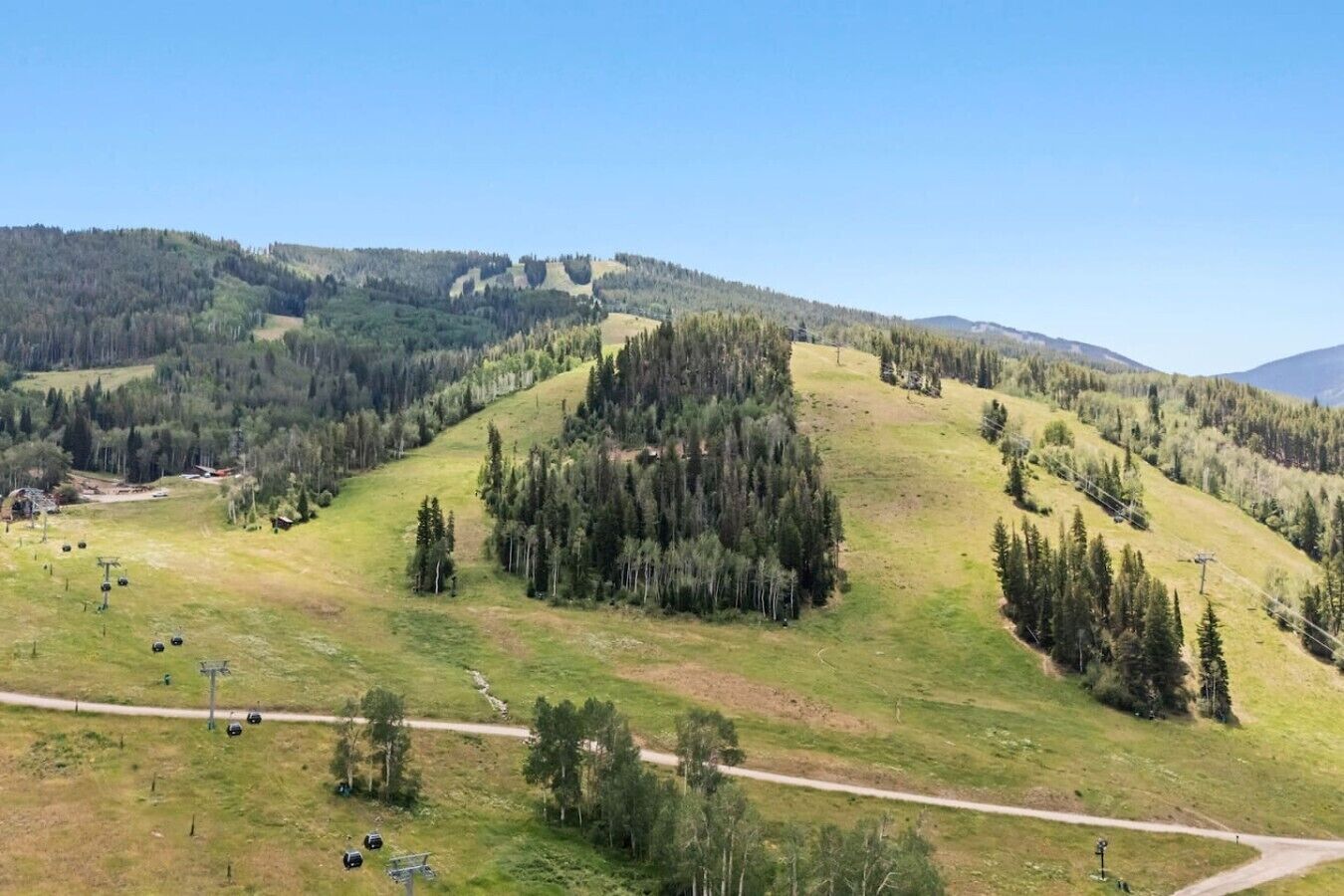 A hilly landscape with a road, trees, and a clear sky.