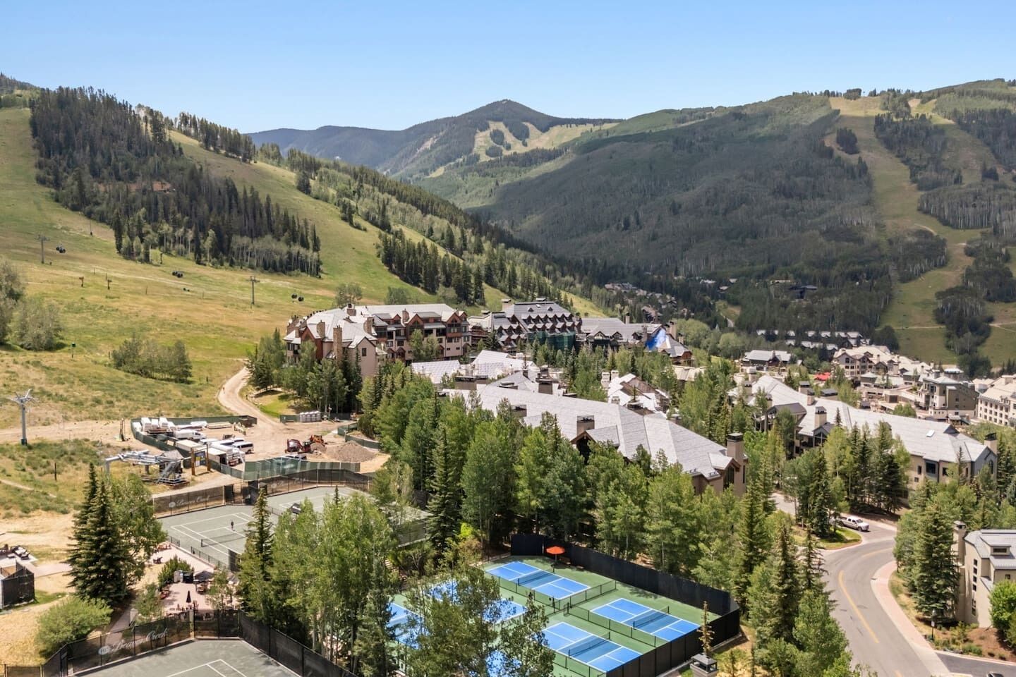 A mountain resort with multiple buildings, a tennis court, and surrounding forested hills.