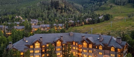 A large lodge with multiple buildings, surrounded by forested hills.