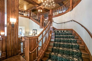 A grand wooden staircase with a chandelier, leading to an upper level with a view of the interior. - Ski-in/ski-out Beaver Creek with Hot Tub & Pool (Beaver Creek)