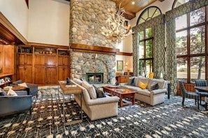 A spacious living room with a stone fireplace, wooden furniture, and large windows. - Ski-in/ski-out Beaver Creek with Hot Tub & Pool (Beaver Creek)
