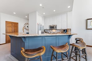 A kitchen with a large island, white cabinets, a clock, and two stools. - Ski-in/ski-out Beaver Creek with Hot Tub & Pool (Beaver Creek)