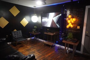 A room with a black and gold wall, a large TV, a black leather sofa, a small table with a plant, and a hanging light fixture. - Cozy 2-bedroom apartment with AC in tranquil Atlanta 8min walk to MB Stadium (Atlanta)