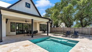 A covered patio area with a swimming pool, stone flooring, and outdoor furniture.