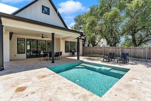 A covered patio area with a swimming pool, stone flooring, and outdoor furniture.