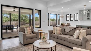 A spacious living room with two sofas, a coffee table, and a dining area visible through glass sliding doors.
