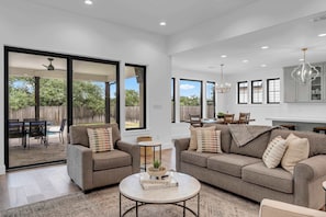 A spacious living room with two sofas, a coffee table, and a dining area visible through glass sliding doors.