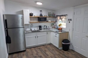 Una cocina compacta con armarios blancos, un refrigerador de acero inoxidable, un microondas y un lavamanos.