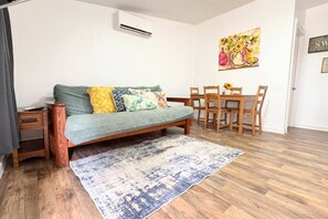 Una sala de estar con un sofá, una mesa de comedor con sillas, una alfombra y un equipo de aire acondicionado.