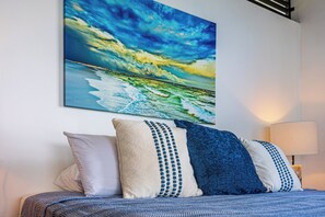 Ein Bett mit einem gemusterten Überwurf, zwei Kissen und einem Wandbild mit einer Strandansicht.