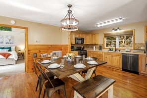 Een moderne keuken met houten kastjes, een eettafel gedekt voor vier personen en een groot raam met uitzicht op bomen.