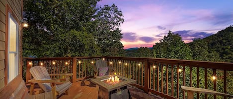 A deck with outdoor seating, a fire pit, and string lights.