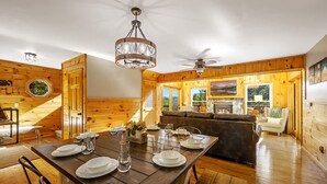 Un intérieur en bois avec une table à manger pour quatre personnes, une cheminée et une vue sur l’extérieur.
