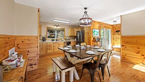 Un intérieur en bois comprenant une table à manger pour quatre personnes, une cuisine avec des meubles en bois, un réfrigérateur et un lustre.
