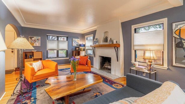 A living room with a fireplace, orange sofas, a wooden coffee table, and a patterned rug. - Stylish Old Reno Home Near Midtown + EV Charger (Reno)