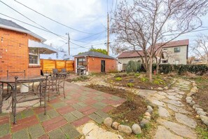Un pati darrere amb terrassa, una petita construcció de maó i una zona de jardí.