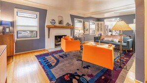 A living room with a fireplace, two orange chairs, a blue sofa, and a patterned rug. - Stylish Old Reno Home Near Midtown + EV Charger (Reno)