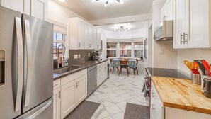 A modern kitchen with stainless steel appliances, white cabinetry, a wooden countertop, and a dining area with a table and chairs. - Stylish Old Reno Home Near Midtown + EV Charger (Reno)