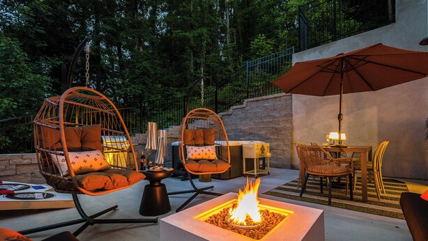 Une terrasse extérieure avec des fauteuils en osier, un foyer et un espace repas comprenant une table et des chaises.