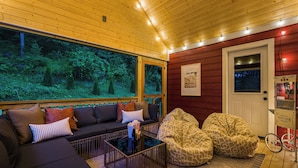 Un intérieur chaleureux avec un plafond en bois, un canapé, des fauteuils en forme de poire et une grande fenêtre donnant sur la forêt.