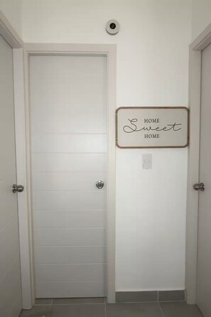 Ein Flur mit einer weißen Tür, einem an der Wand befestigten Schild mit der Aufschrift 'Sweet Home HOME' und einem Lichtschalter.