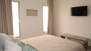 Quarto com cama, uma mesinha, TV fixada na parede e um letreiro na parede.