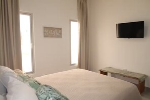Ein Schlafzimmer mit einem Bett, einem kleinen Tisch, einem Wandfernseher und einem Wandzeichen.