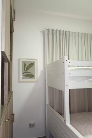 Ein Stockbett mit weißem Gestell und einer Matratze, ein gerahmtes Bild an der Wand und eine Tür mit Griff.