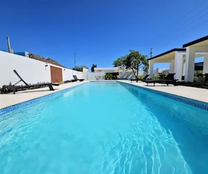 Ein klares, blaues Schwimmbecken mit Liegestühlen und ein weißes Gebäude im Hintergrund.