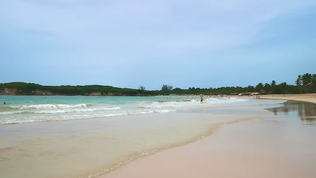 Uma praia com extensa faixa de areia e ondas suaves.
